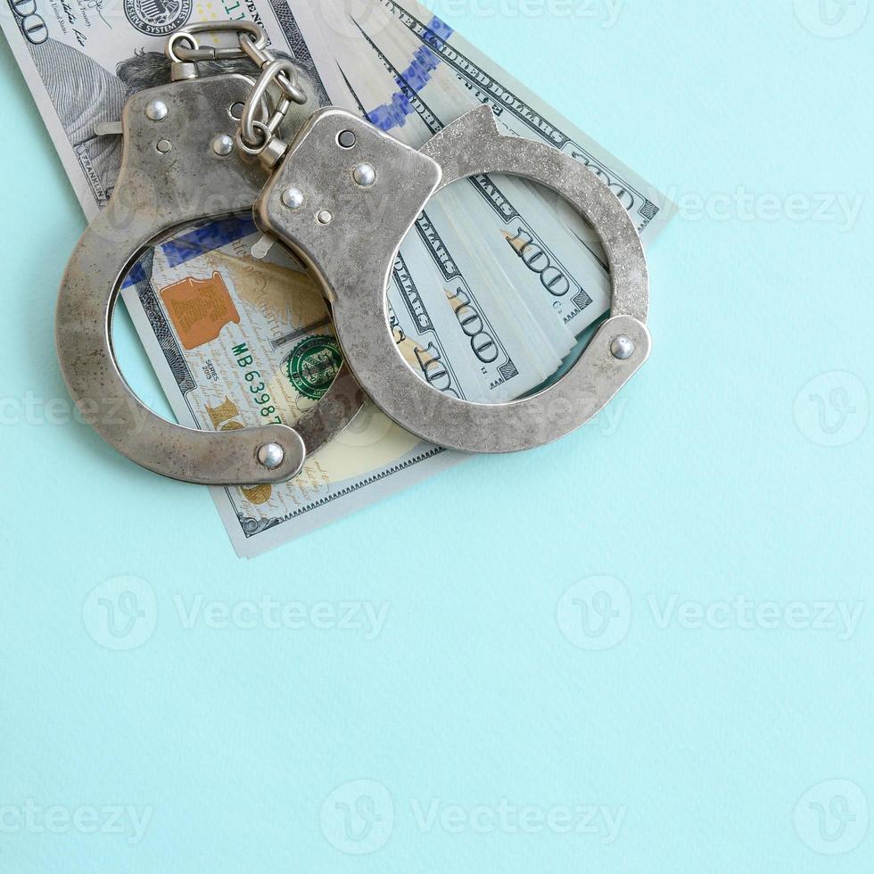 esposas de policía plateadas y billetes de cien dólares sobre fondo azul claro foto