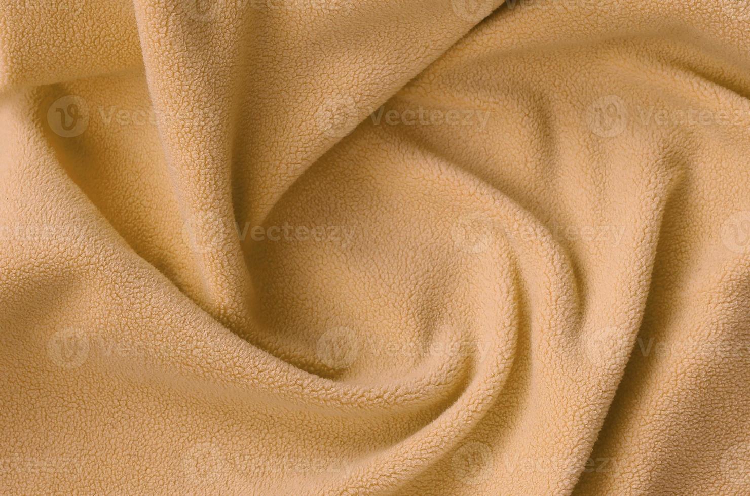 The blanket of furry orange fleece fabric. A background of light orange soft plush fleece material with a lot of relief folds photo