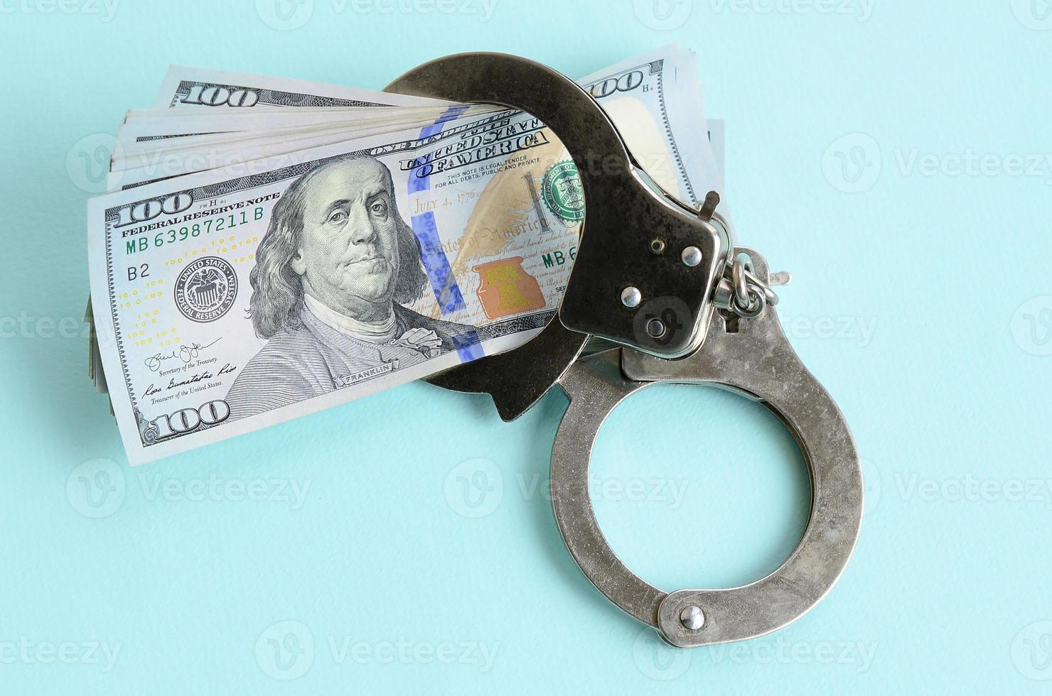 Silver police handcuffs and hundred dollar bills lies on light blue background photo