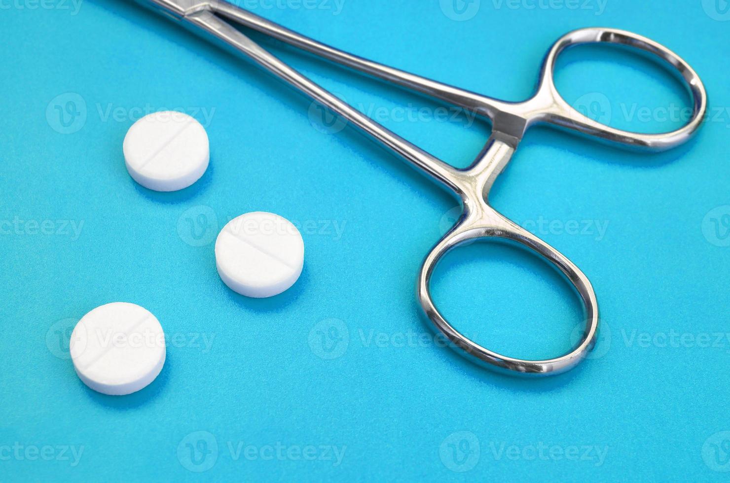 Several white tablets and a medical clamp lie on a bright blue background surface. Background image on medical and pharmaceutical topics photo