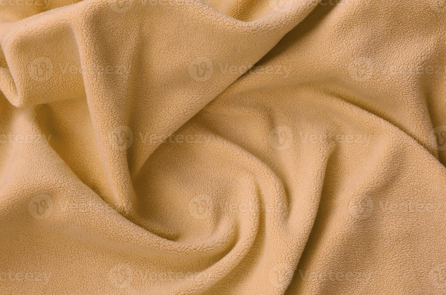 The blanket of furry orange fleece fabric. A background of light orange soft plush fleece material with a lot of relief folds photo
