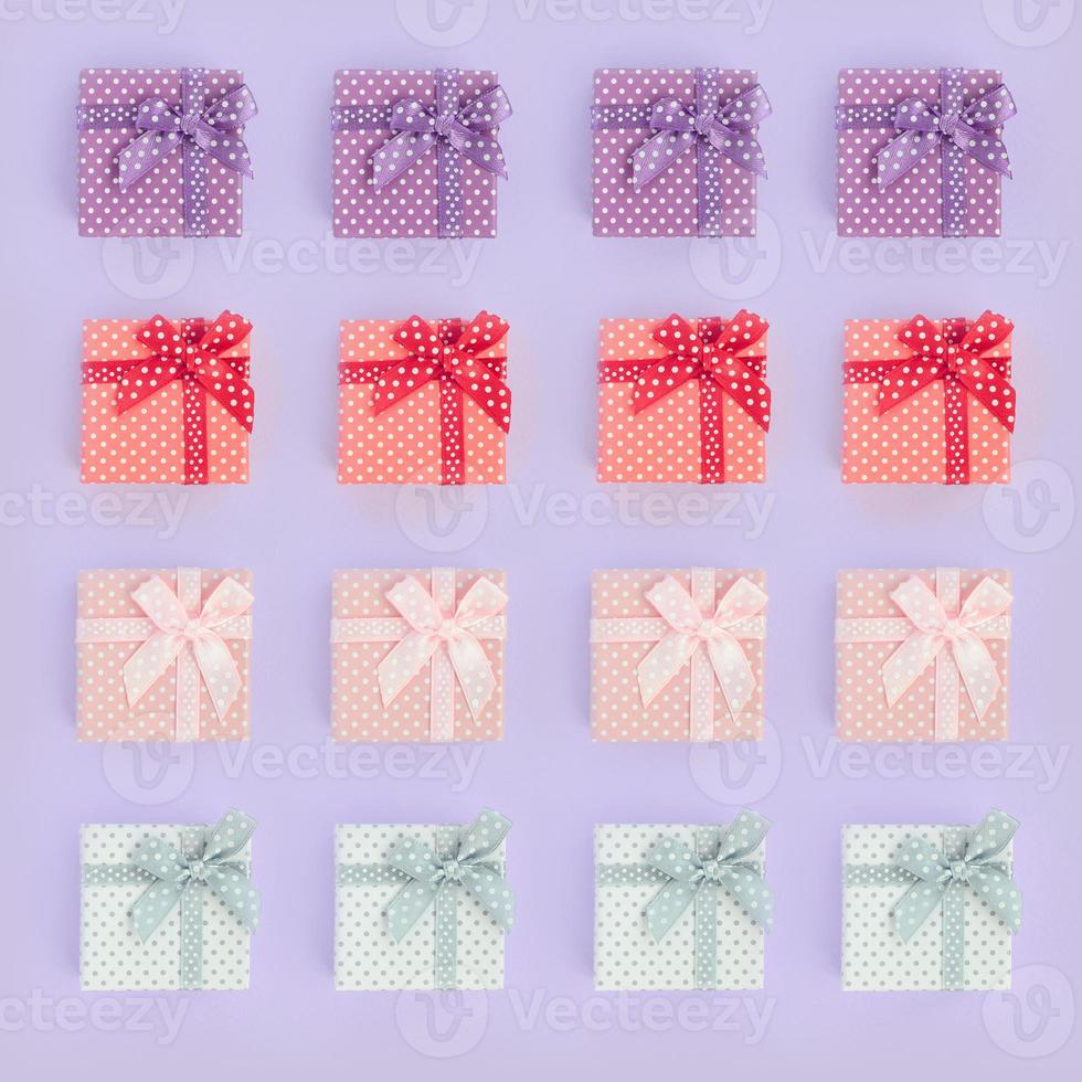 Piles of a small colored gift boxes with ribbons lies on a violet background. Minimalism flat lay top view pattern photo