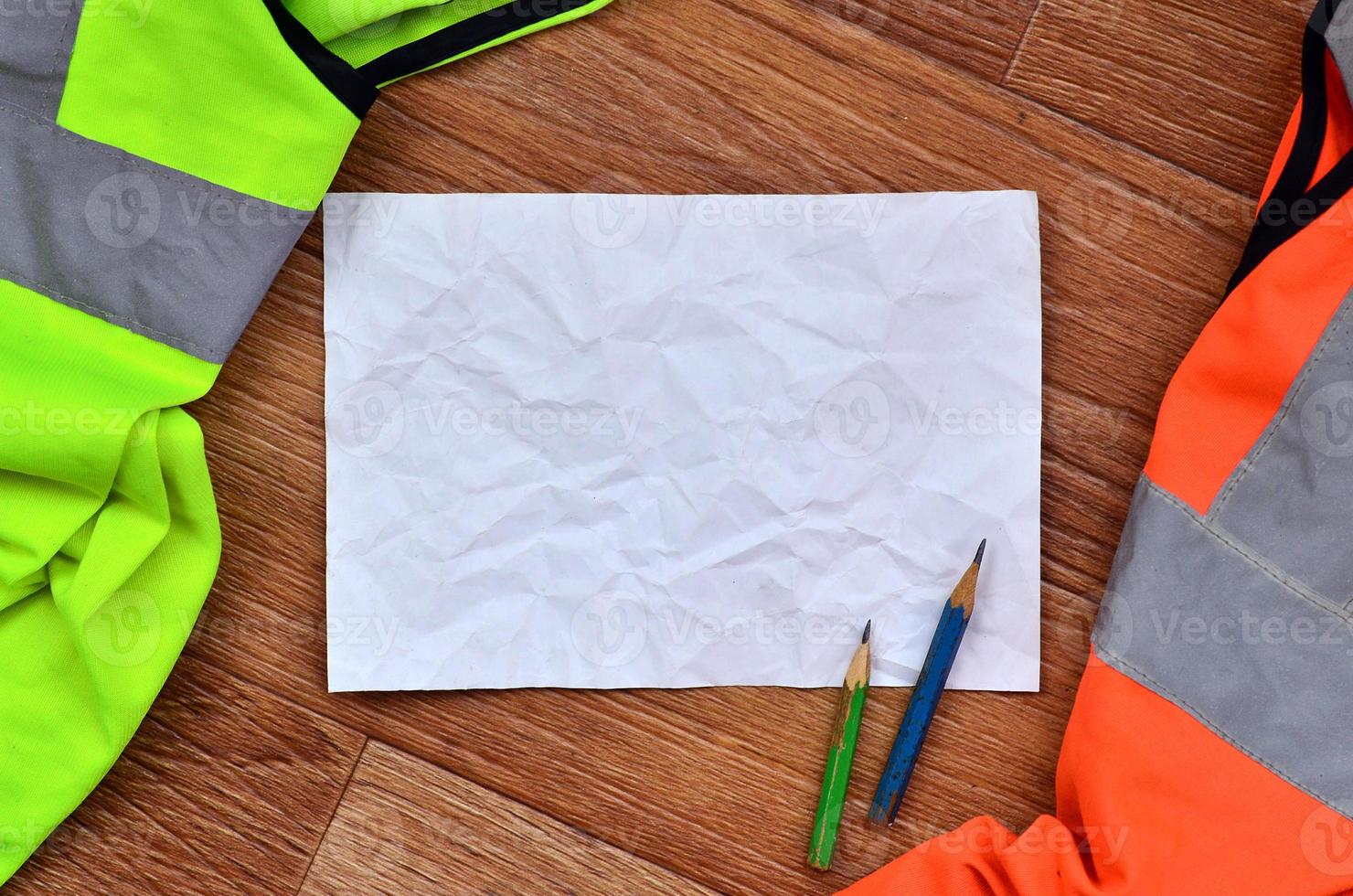 A crumpled sheet of paper with two pencils surrounded by green a photo