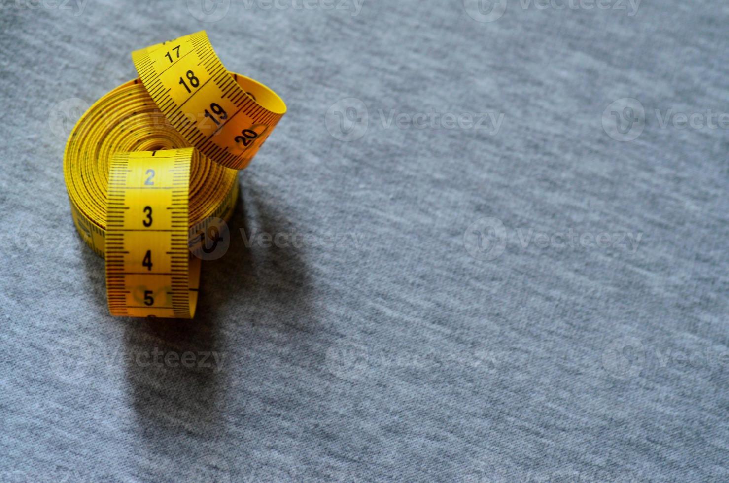 Yellow measuring tape lies on a gray knitted fabric photo