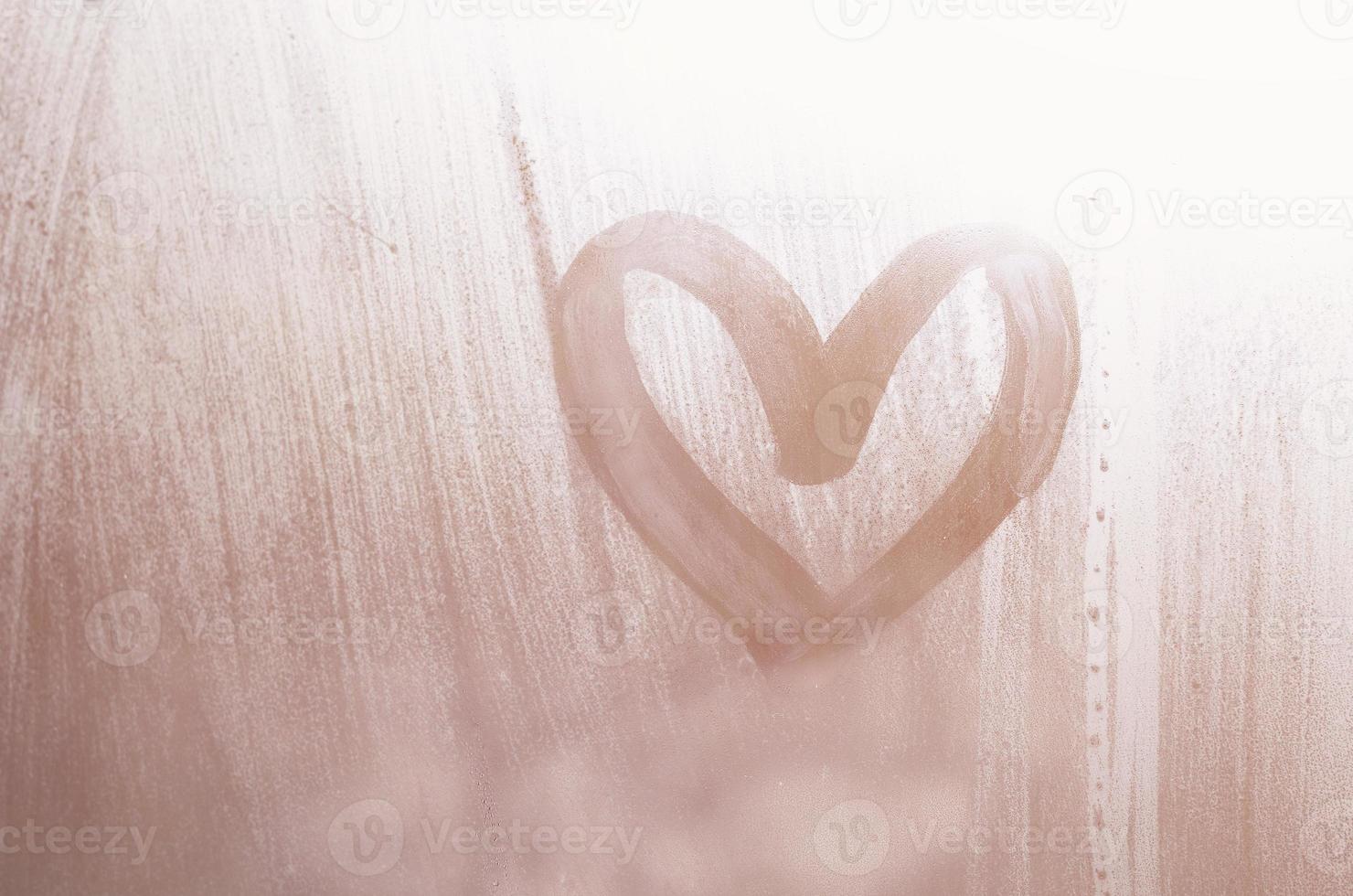 A heart-shaped drawing drawn by a finger on a misted glass in rainy weather photo