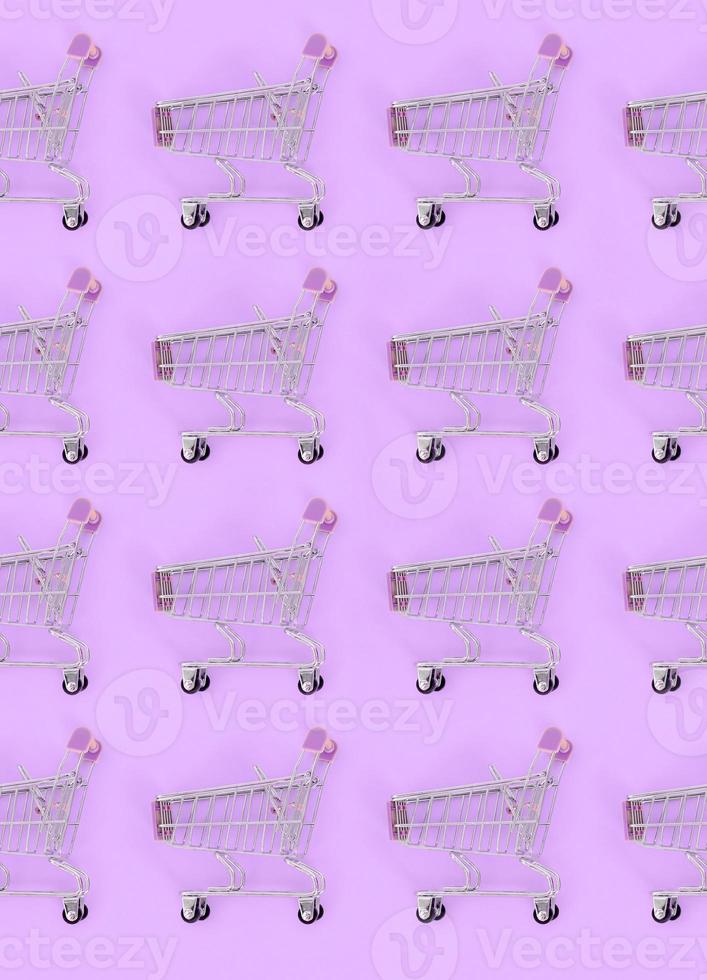 Shopping addiction, shopping lover or shopaholic concept. Many small empty shopping carts perform a pattern on a pastel colored paper background. Flat lay composition, top view photo