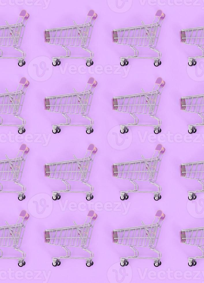 Shopping addiction, shopping lover or shopaholic concept. Many small empty shopping carts perform a pattern on a pastel colored paper background. Flat lay composition, top view photo