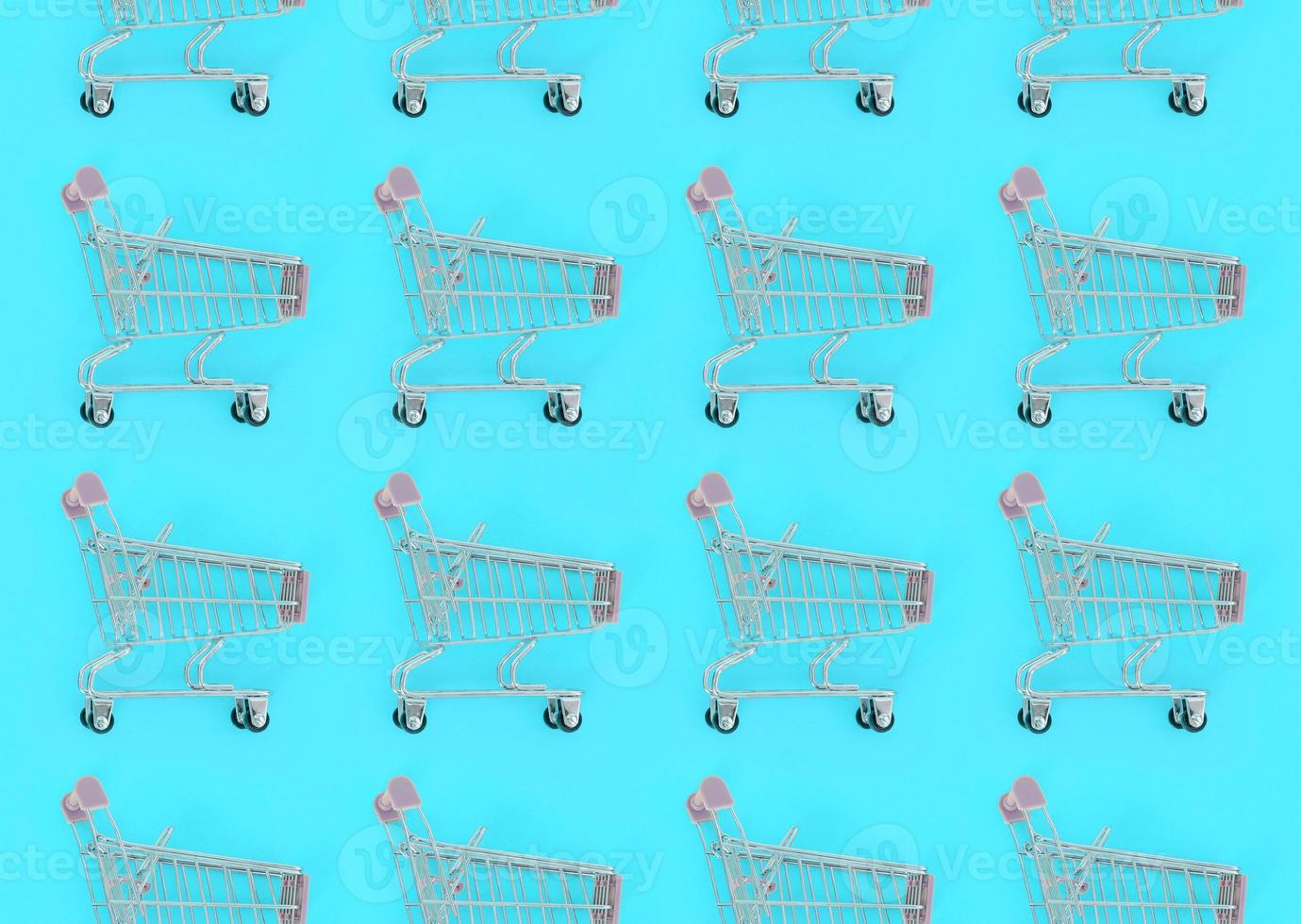 Shopping addiction, shopping lover or shopaholic concept. Many small empty shopping carts perform a pattern on a pastel colored paper background. Flat lay composition, top view photo