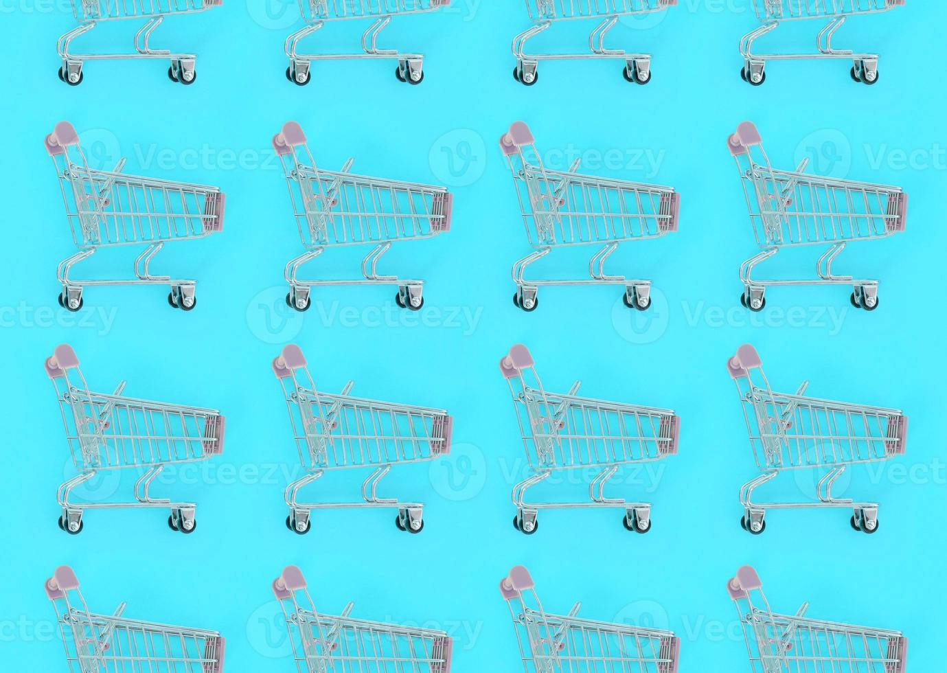 Shopping addiction, shopping lover or shopaholic concept. Many small empty shopping carts perform a pattern on a pastel colored paper background. Flat lay composition, top view photo