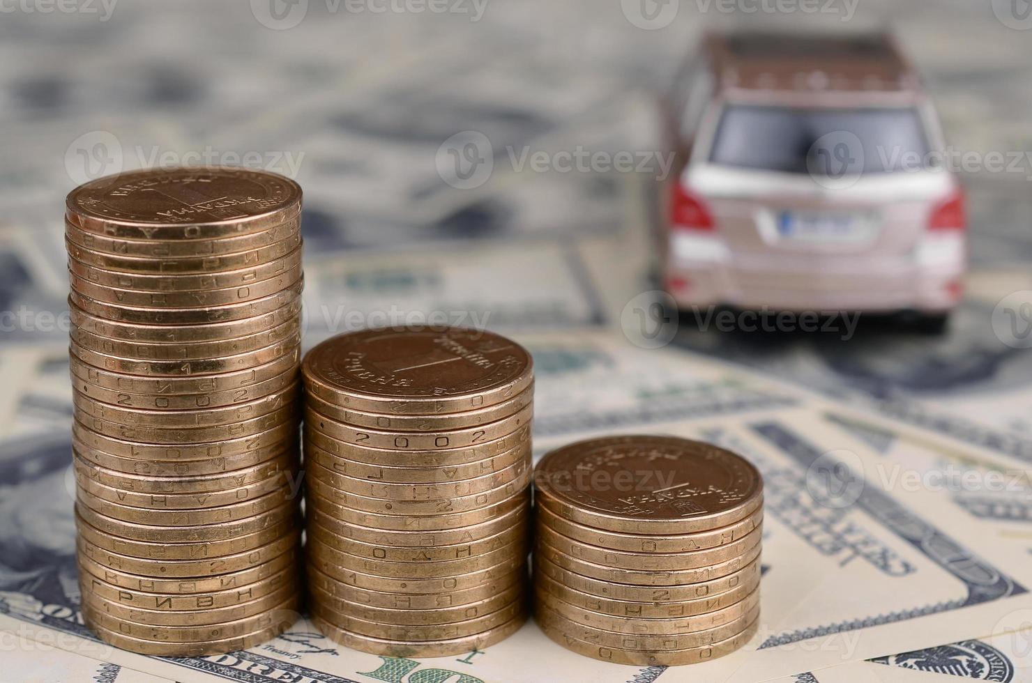 Toy car model at the stacks of golden coins lies on many dollar bills photo