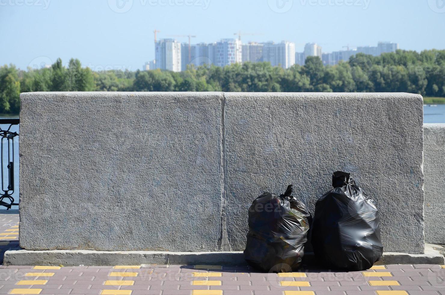 Two black garbage bags on tiled street floor at concrete fence in city photo