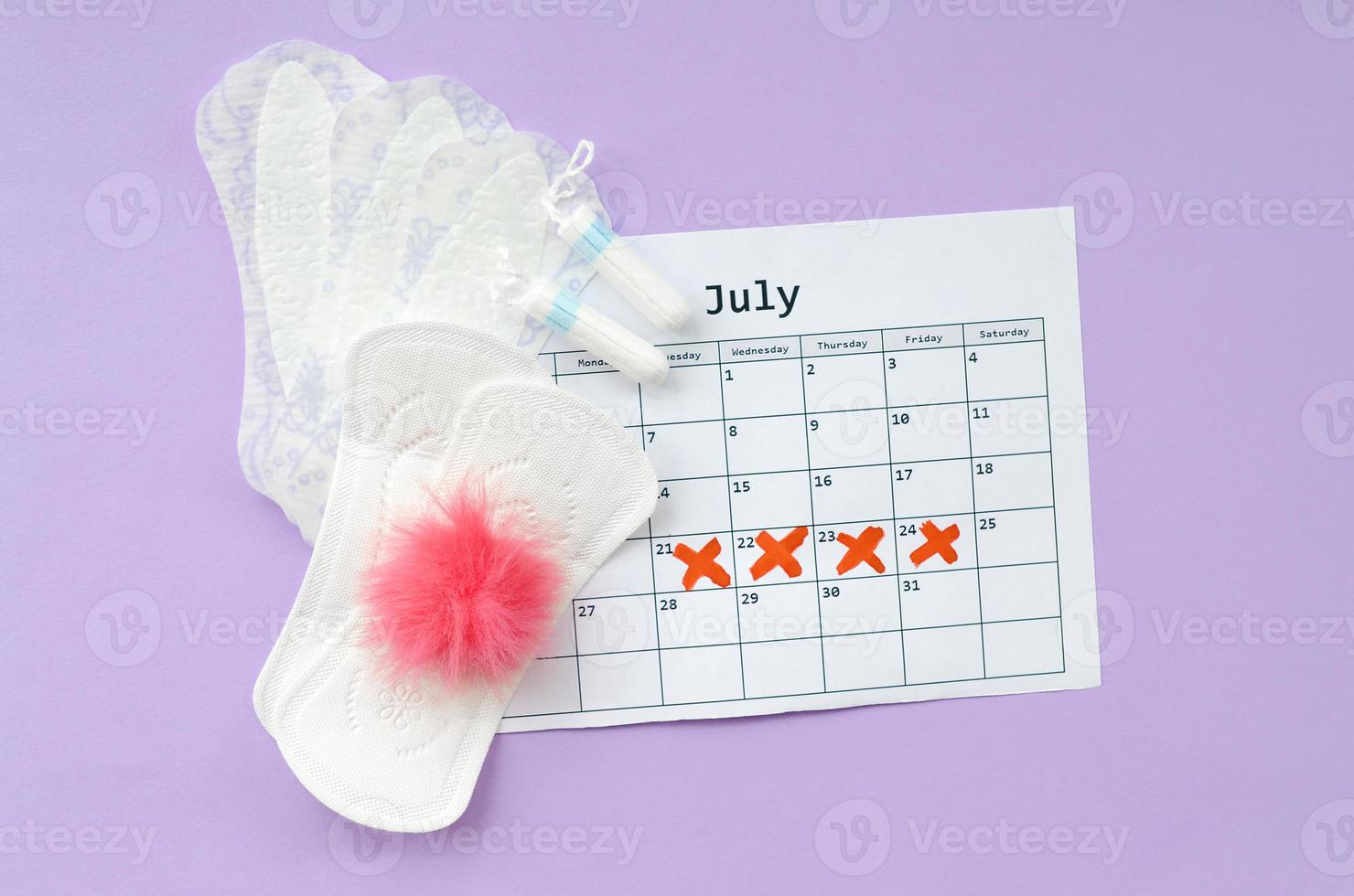 Menstrual pads and tampons on menstruation period calendar flat lay on lilac background photo