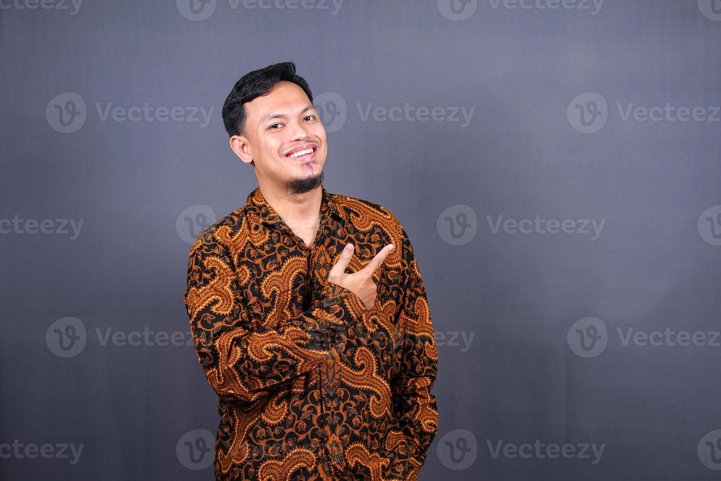 retrato de un joven feliz en batik indonesia señalando con el dedo el espacio de copia aislado sobre fondo gris foto