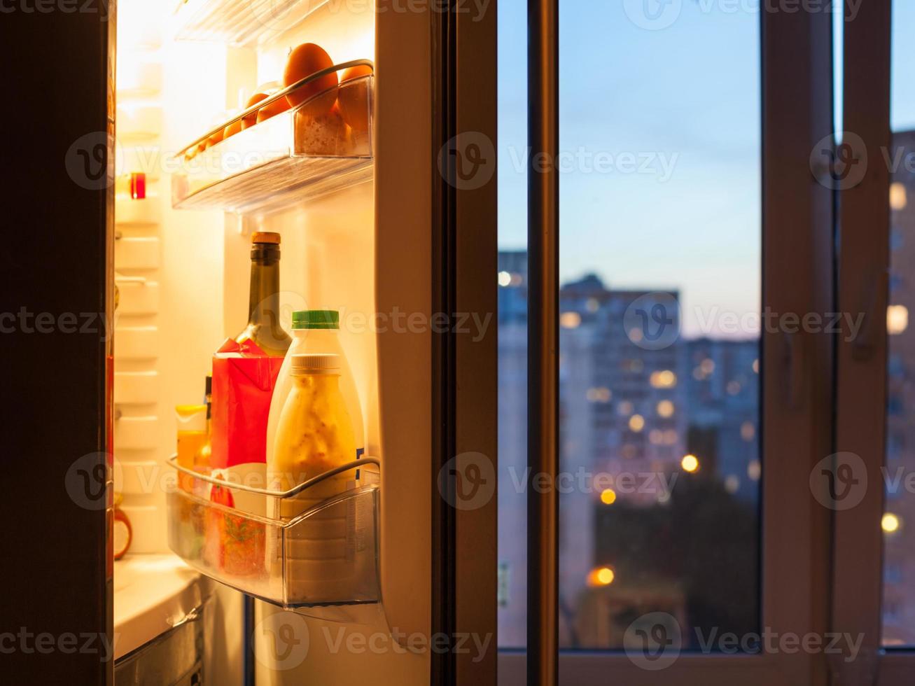 Open door of refrigerator with food in evening photo