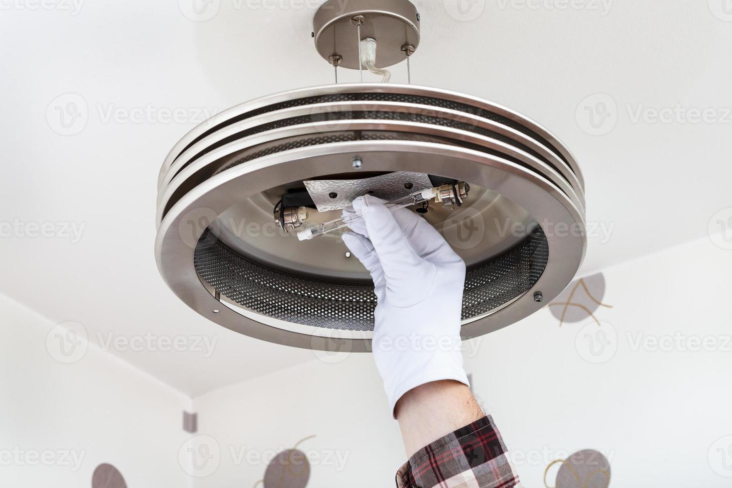 electricista monta una lámpara halógena en la luz del techo foto
