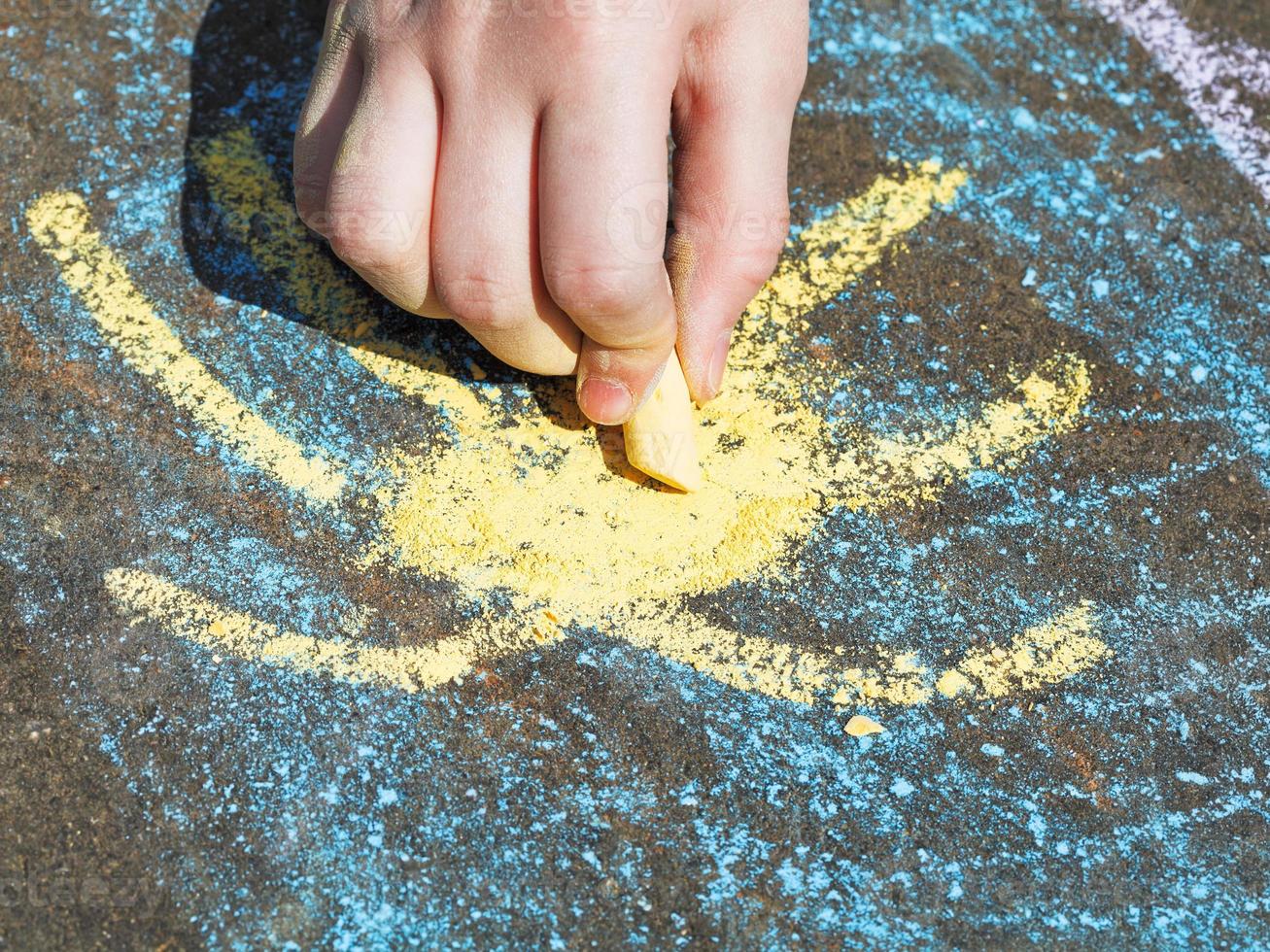 girl drawing yellow sun in blue sky with chalks photo