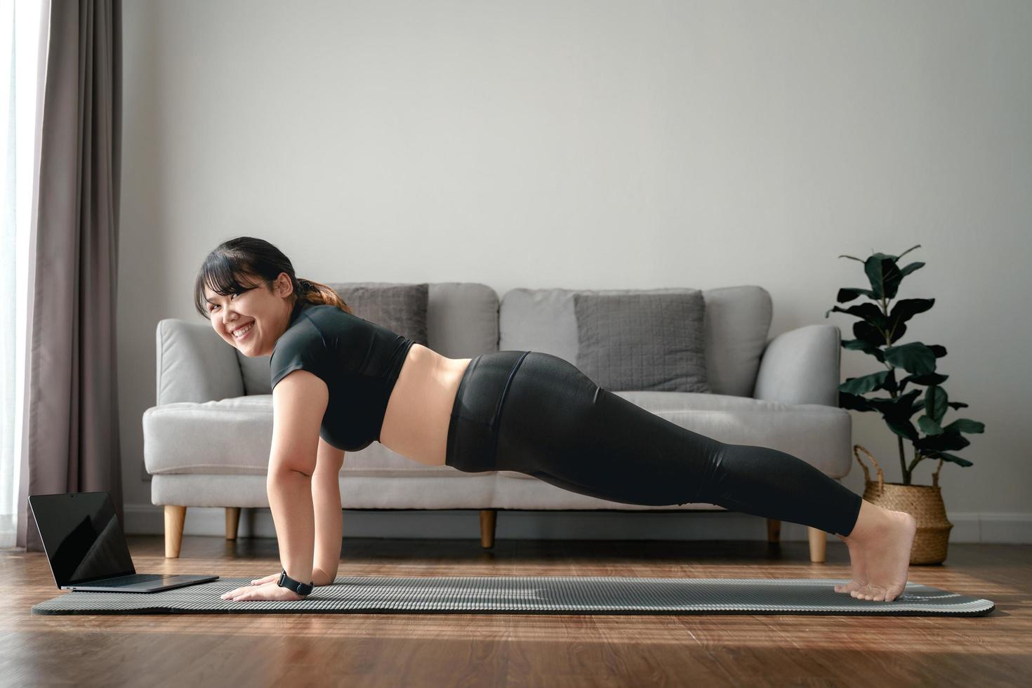 mujer gordita asiática en la sala de estar practica una lección de yoga en línea con la computadora. mujer con clase de entrenamiento de meditación en la computadora portátil. foto