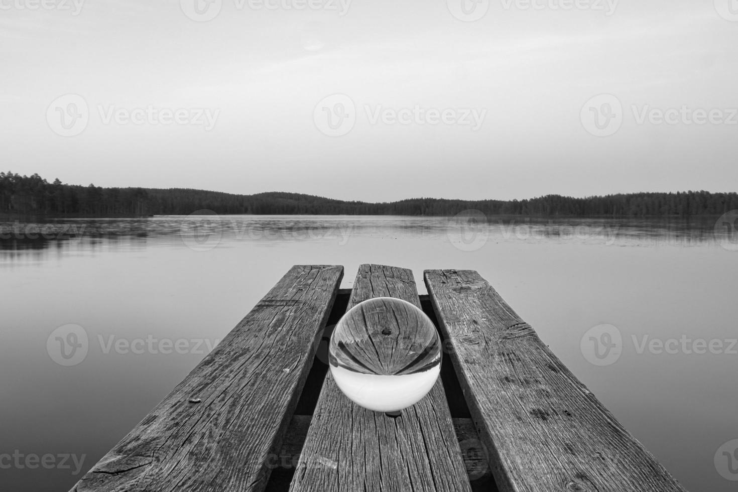 Glass ball on a wooden pier at a Swedish lake at dusk in black and white. Nature photo