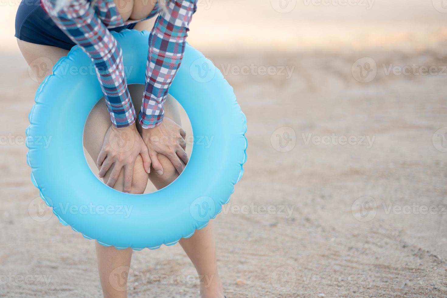 Woman in one-piece swimsuit with blue inflatable ring on tropical beach. photo