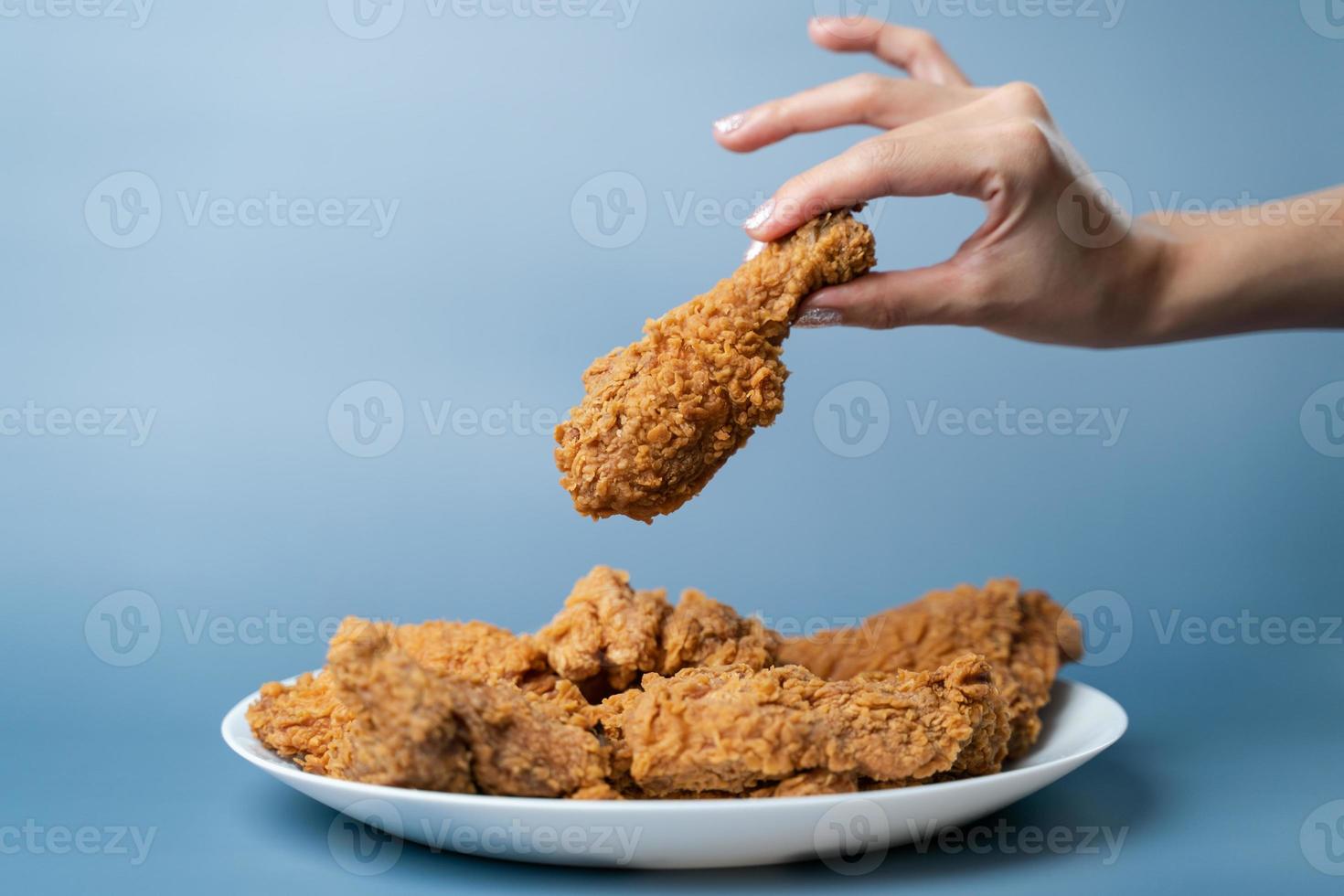 mano sosteniendo baquetas, pollo frito crujiente en plato blanco sobre fondo azul. foto