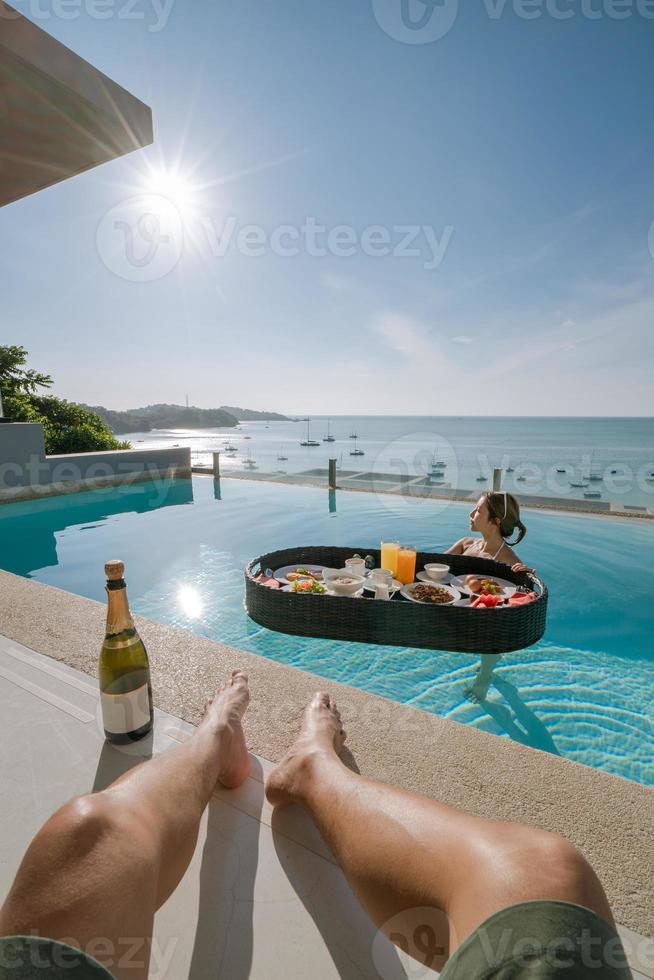 Boyfriend leg with girlfriend relax with floating breakfast in swimming pool villa hotel resort. photo
