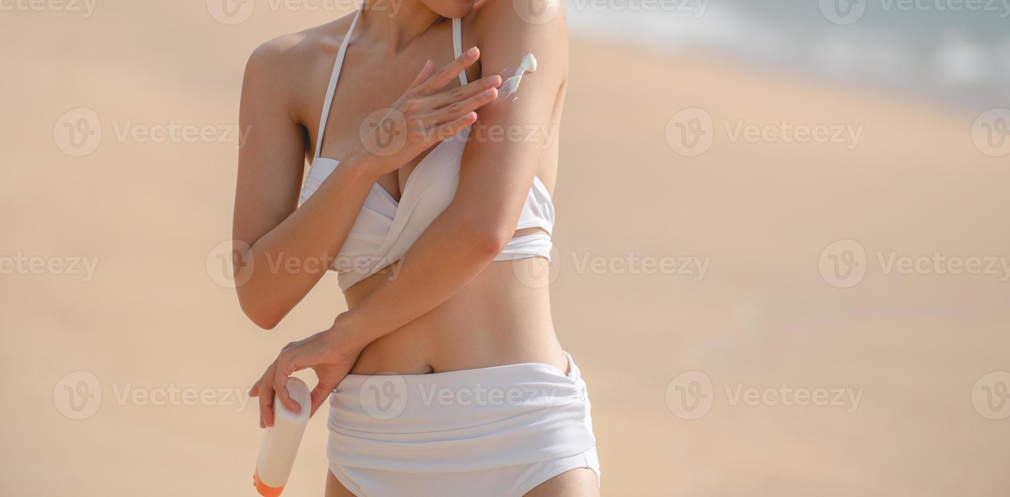 Woman applying Sunscreen in her body on the beach. photo