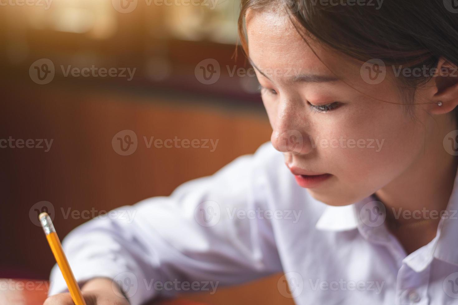 Closeup shot of women student face looking focus in a book with pencil on the table and orange light white empty paper, study and education concept copy space for text and design photo