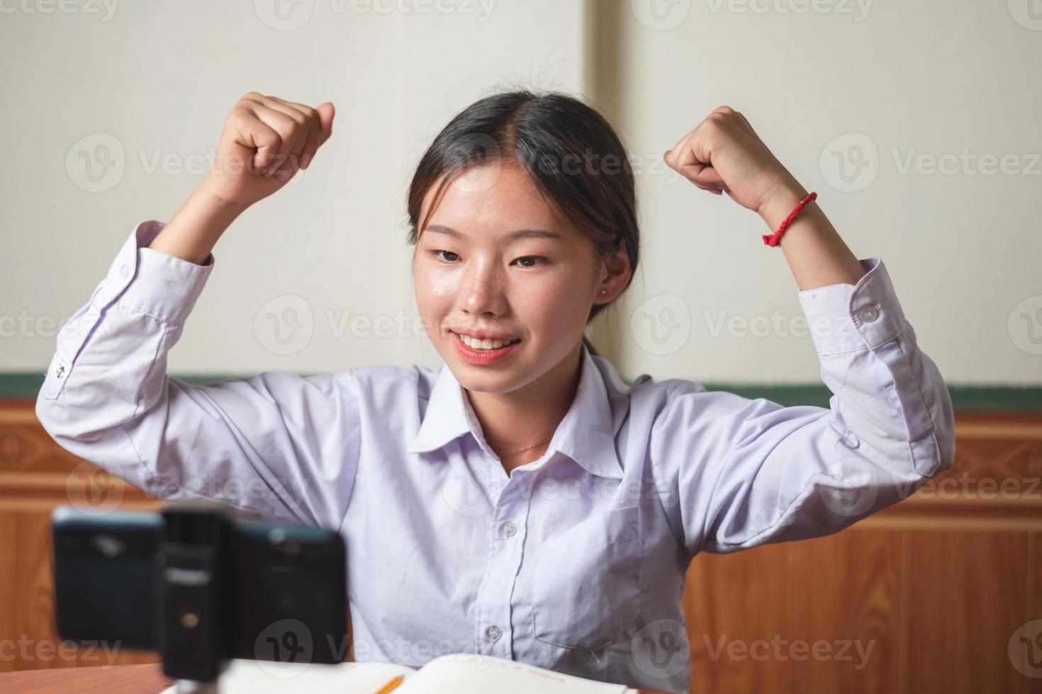 A student girl with white shirt student suit is happy with her winner successful exam result front of the smartphone at home, education and success concept copy space for individual text and design photo