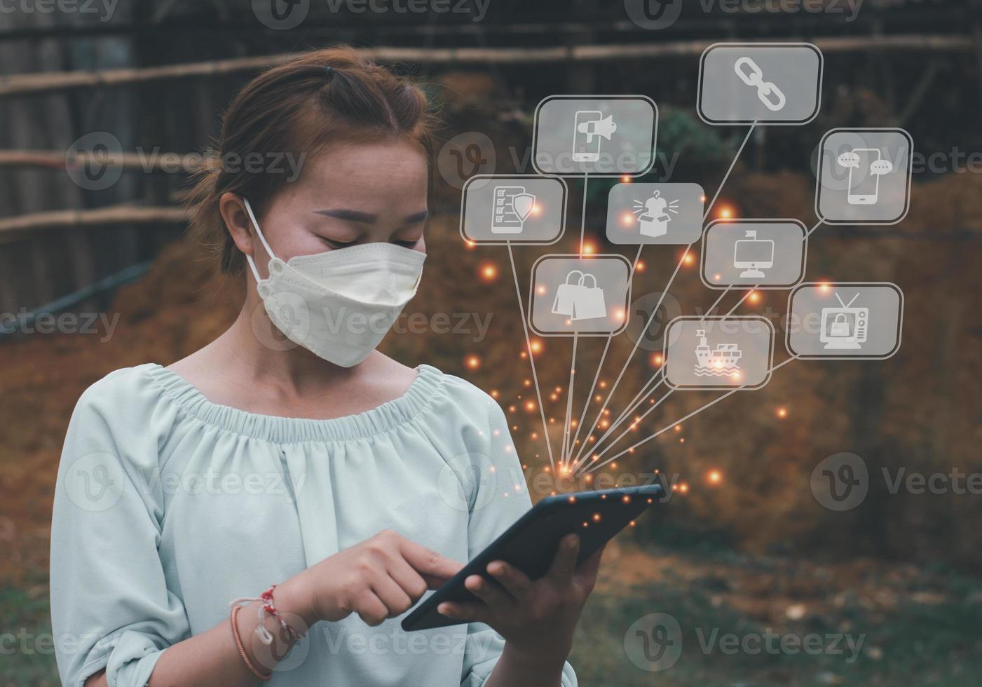una mujer la máscara toca la tableta revisa su negocio con un icono de comercio electrónico vectorial, luz gráfica y fondo borroso foto