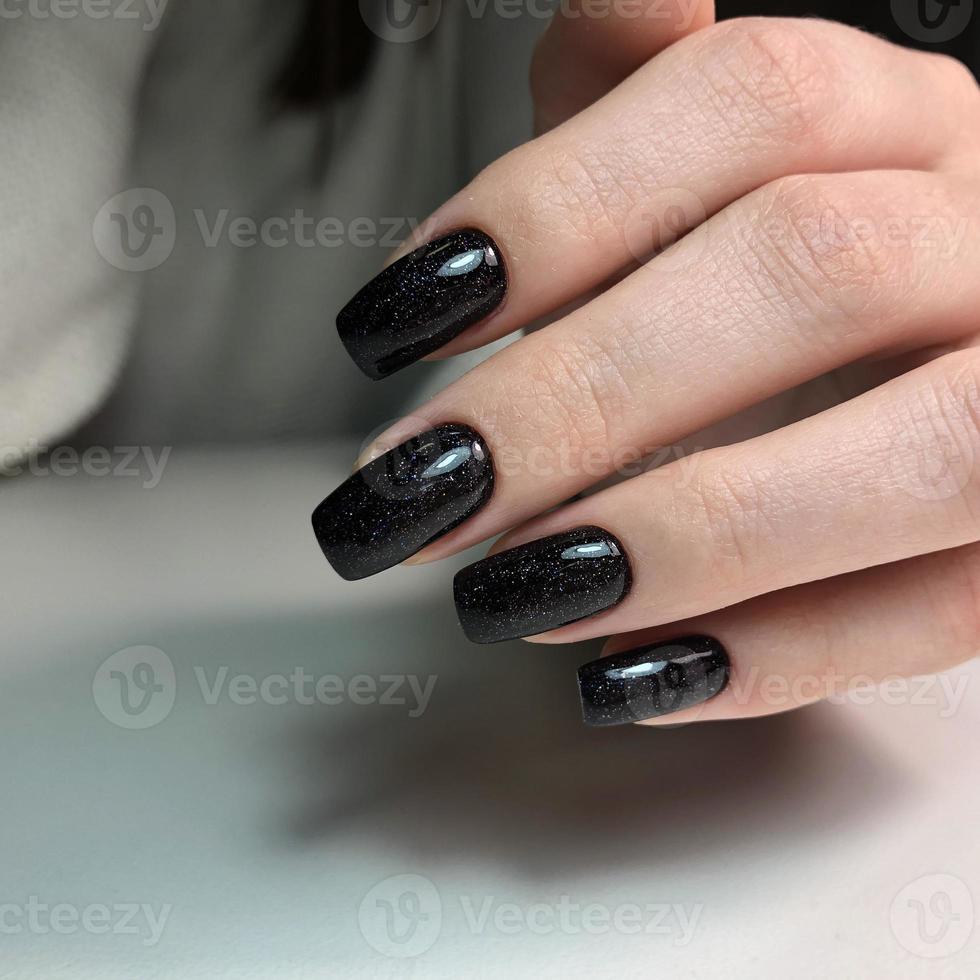 elegante manicura femenina negra de moda. manos de una mujer con manicura negra en las uñas foto