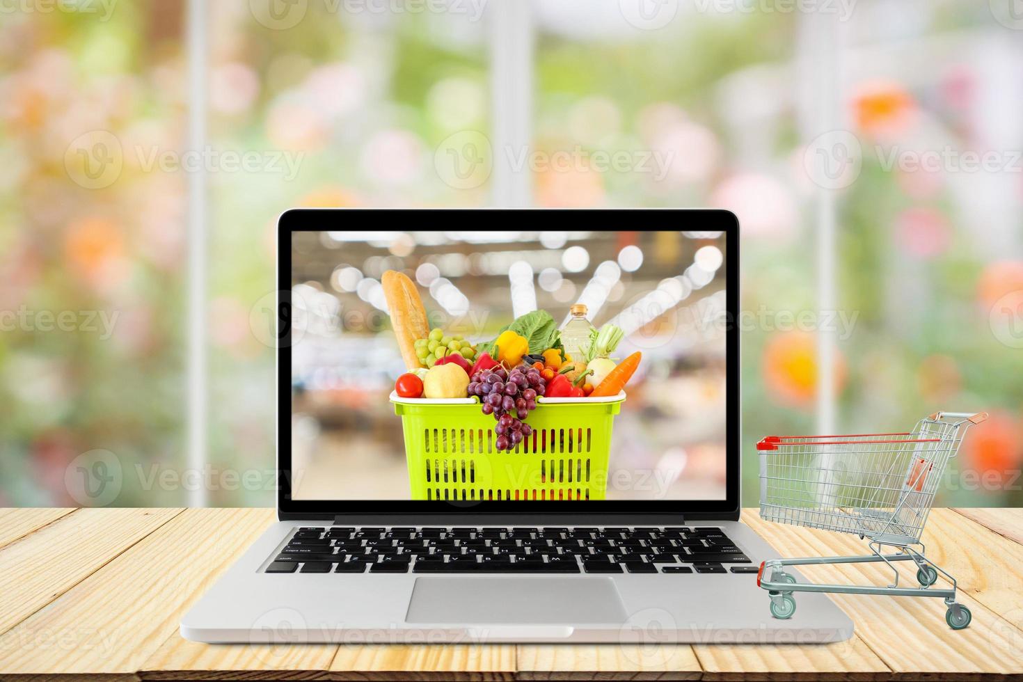 laptop computer and shopping cart on wood table with window and garden abstract blur background grocery online concept photo