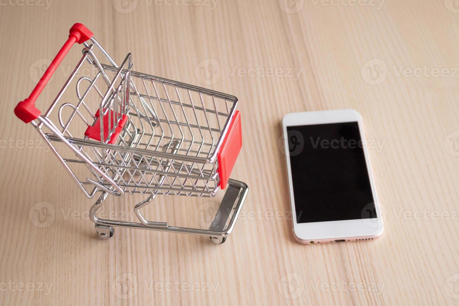 teléfono móvil con carrito de compras en el fondo de la mesa de madera concepto de compras en línea foto