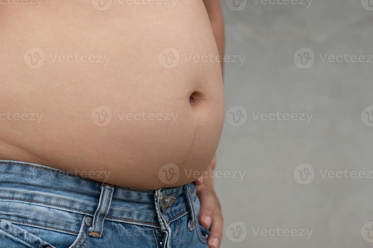 Closeup shot of asian man overweight stomach with jean trousers and cement blur background, planning exercise and loss weight for good health in the feature, healthcare and gym concept copy space photo