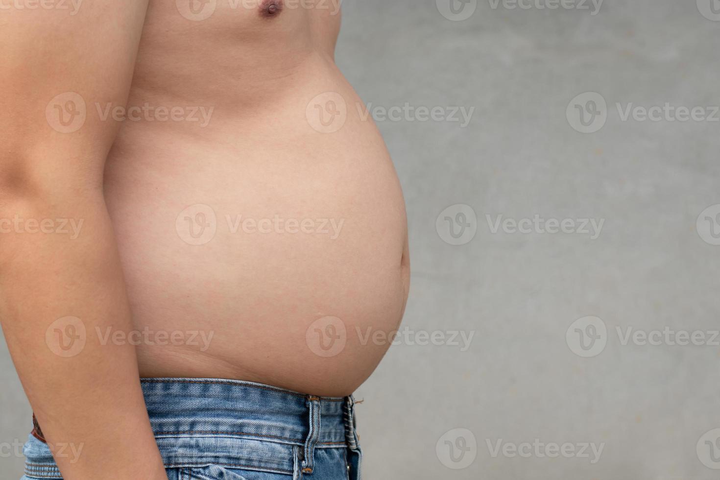 Captura de pantalla de un hombre asiático con sobrepeso en el estómago con pantalones de mezclilla y fondo borroso de cemento, ejercicio de planificación y pérdida de peso para una buena salud en el espacio de copia del concepto de función, atención médica y gimnasio foto