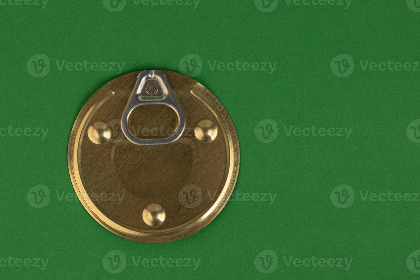 Tin can lid with opener, golden color on a green background. photo