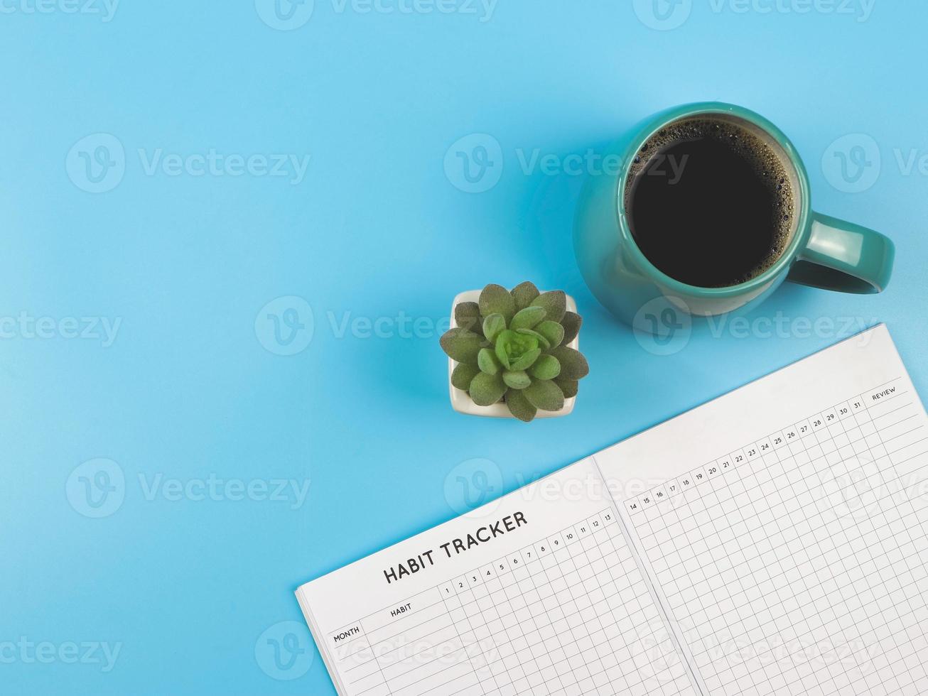 flat lay of habit tracker book with  blue  cup of black coffee and succulent plant pot on blue background with copy space. photo