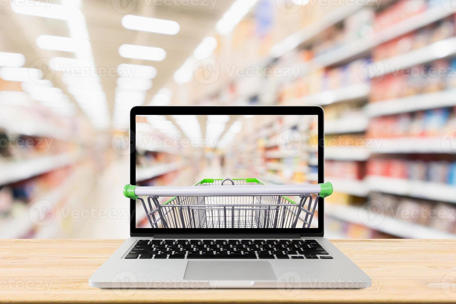 supermarket aisle blurred background with laptop computer and shopping cart on wood table grocery online concept photo