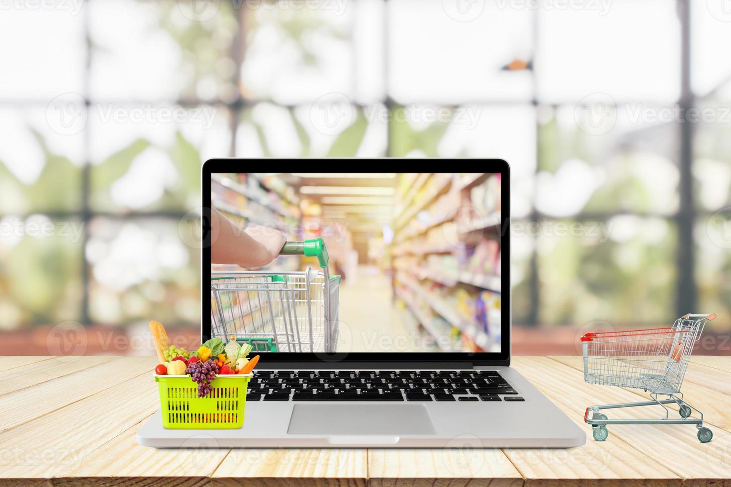 laptop computer and shopping cart on wood table with window and garden abstract blur background grocery online concept photo