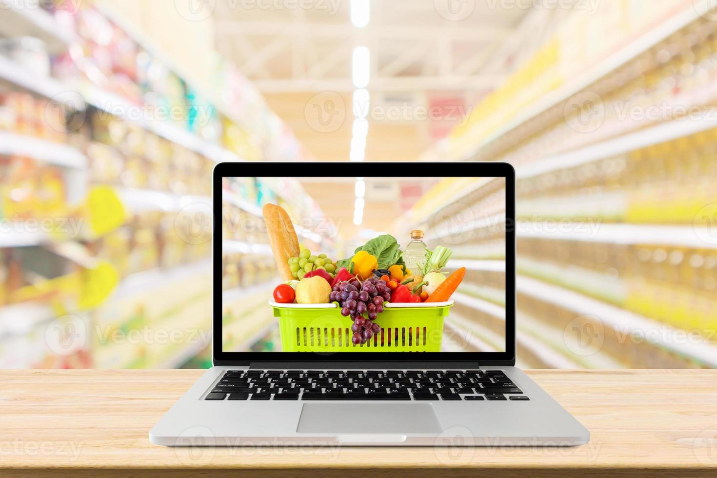 supermarket aisle blurred background with laptop computer and shopping cart on wood table grocery online concept photo