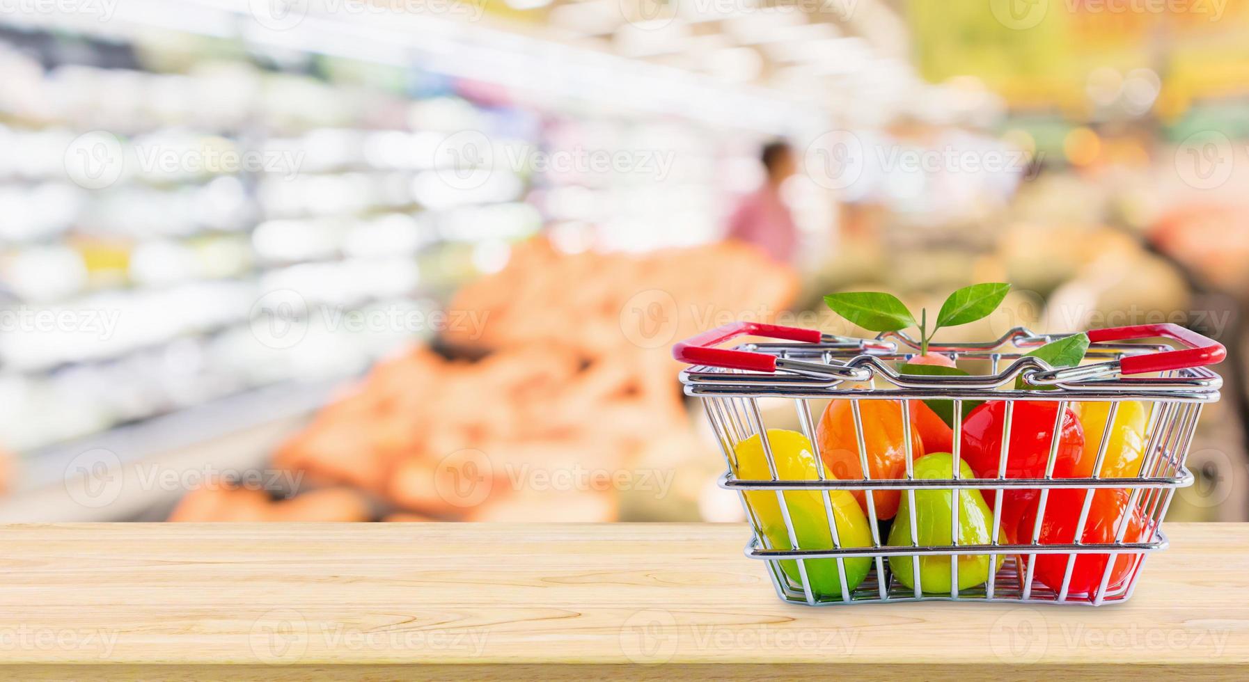 Shopping basket with fruits on wood table over grocery store supermarket blur background photo
