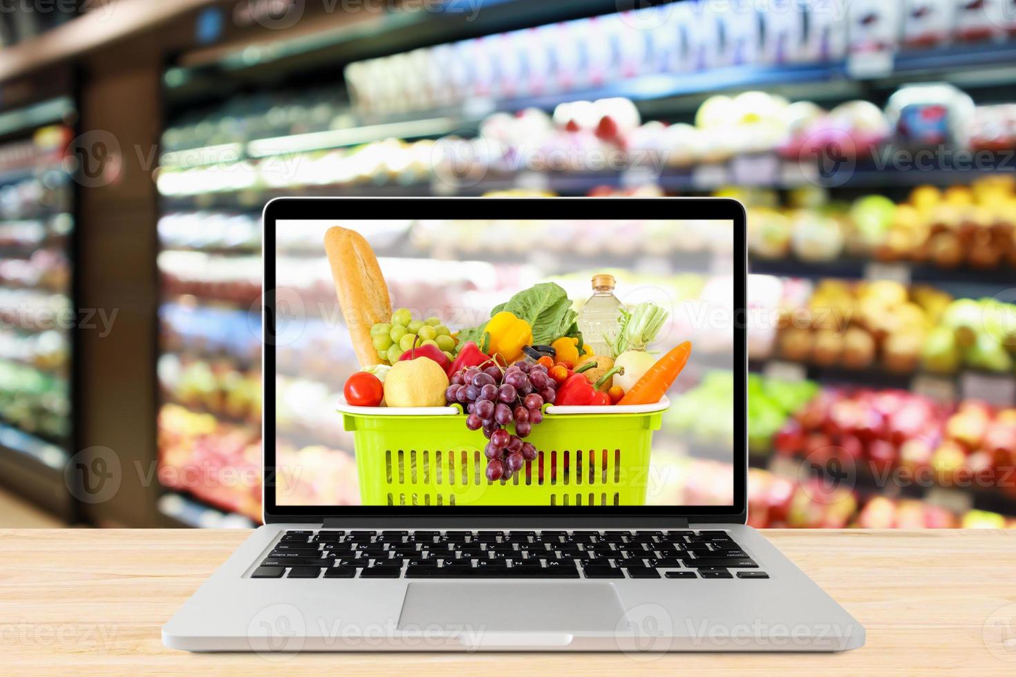 supermarket aisle blurred background with laptop computer and shopping basket on wood table grocery online concept photo