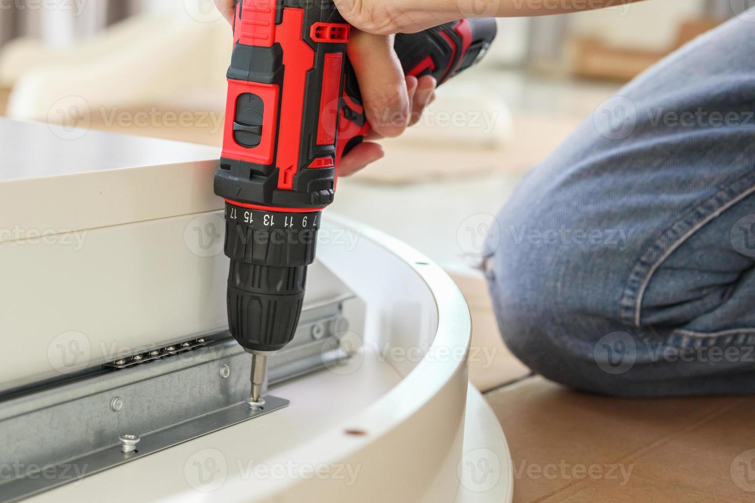 man assembling white table furniture at home using cordless screwdriver photo