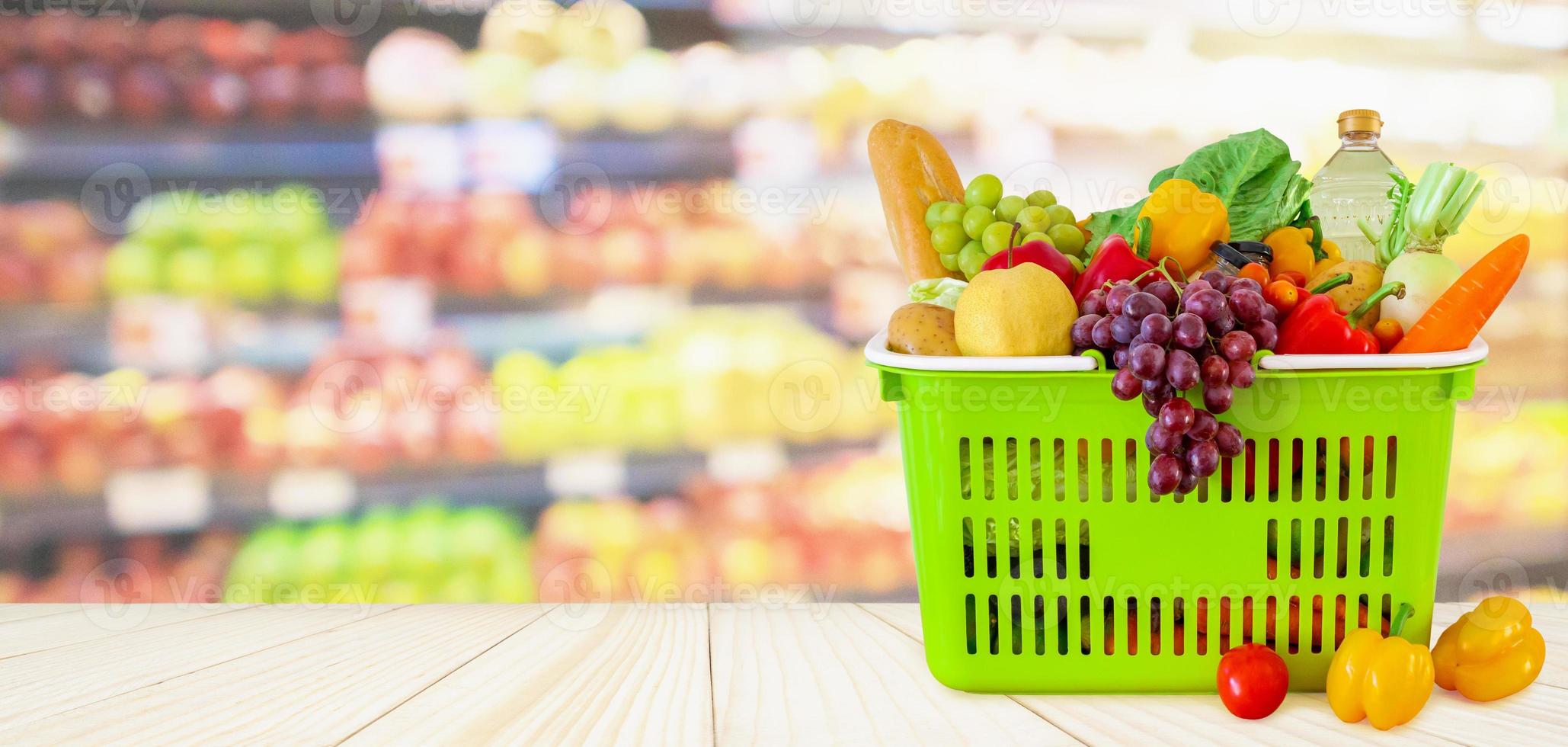 Shopping basket filled with fruits and vegetables on wood table with supermarket grocery store blurred defocused background with bokeh light photo