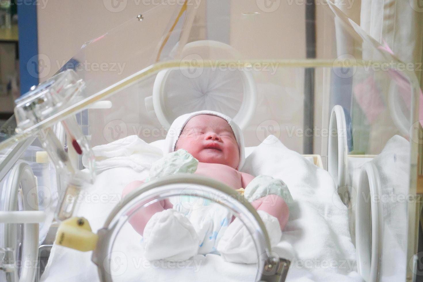 Newborn baby girl inside incubator in hospital post delivery room photo