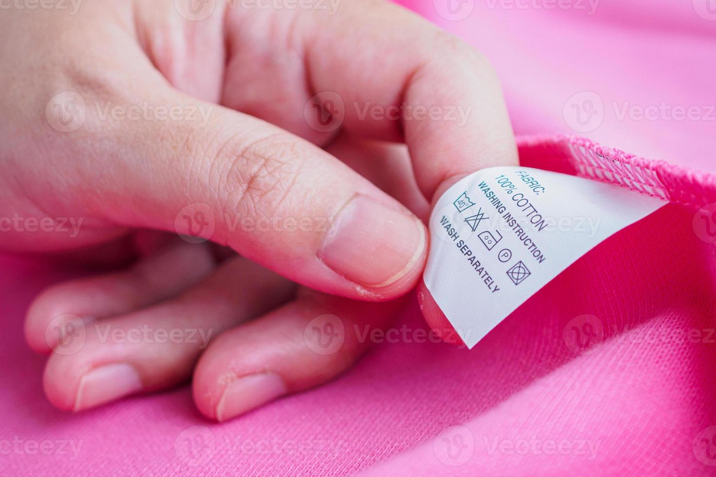 mujer leyendo sobre el cuidado de la ropa instrucciones de lavado etiqueta de ropa en camisa de algodón rosa foto