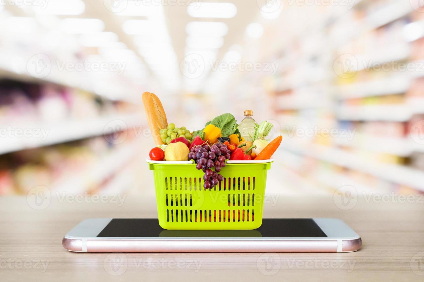 Fresh food and vegetables in shopping basket on mobile smartphone on wood table with supermarket aisle blurred background grocery online concept photo