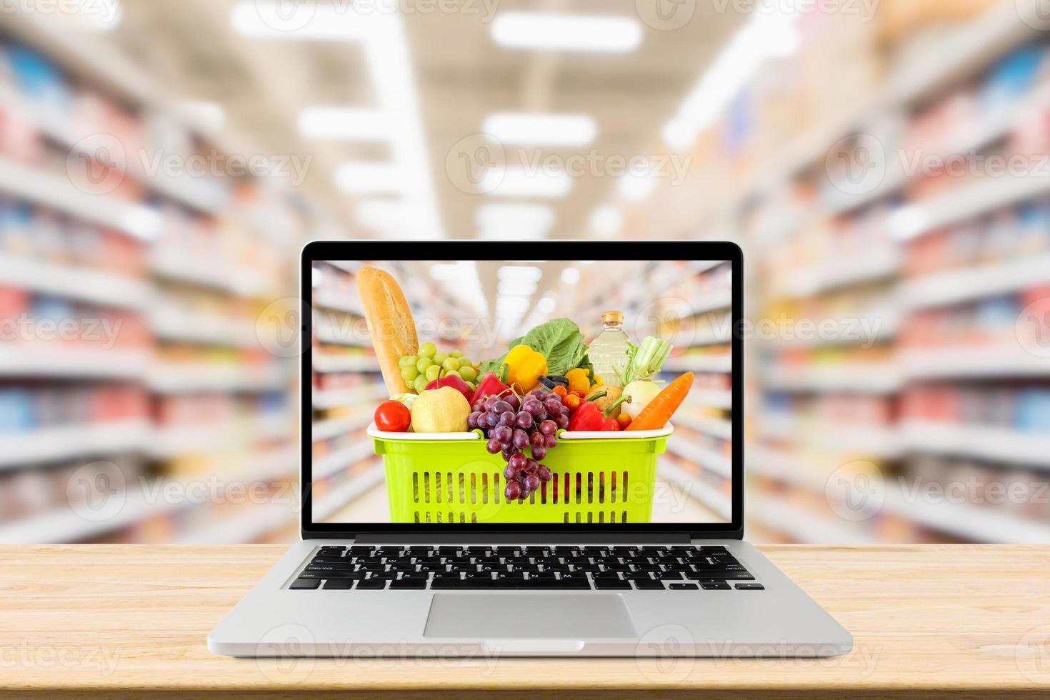 supermarket aisle blurred background with laptop computer and shopping basket on wood table grocery online concept photo