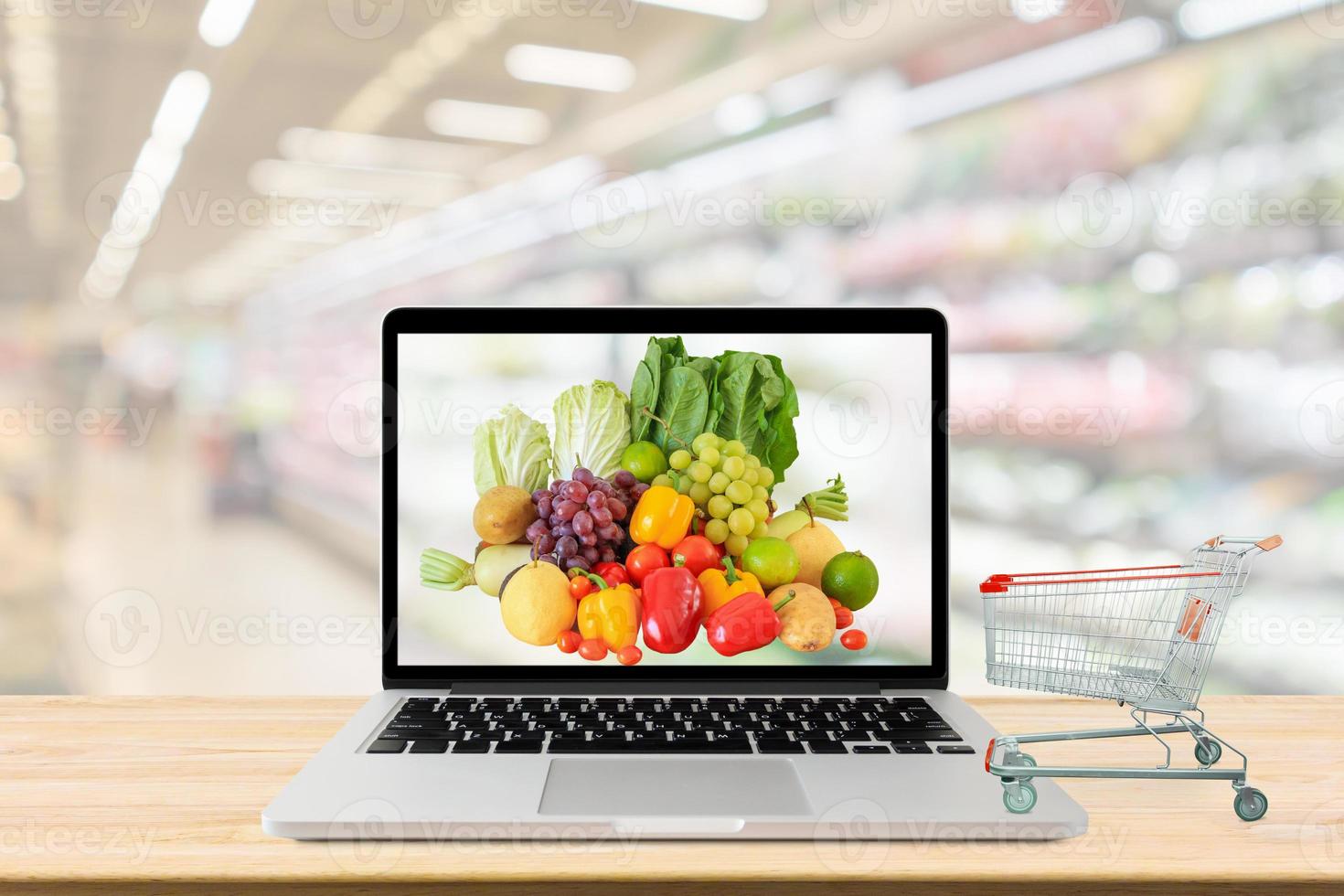 supermarket aisle blurred background with laptop computer and shopping cart on wood table grocery online concept photo