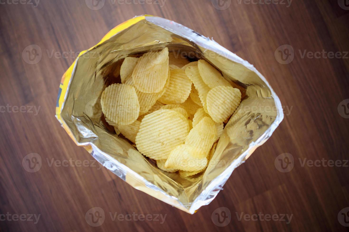 Potato chips in open snack bag close up on table floor photo
