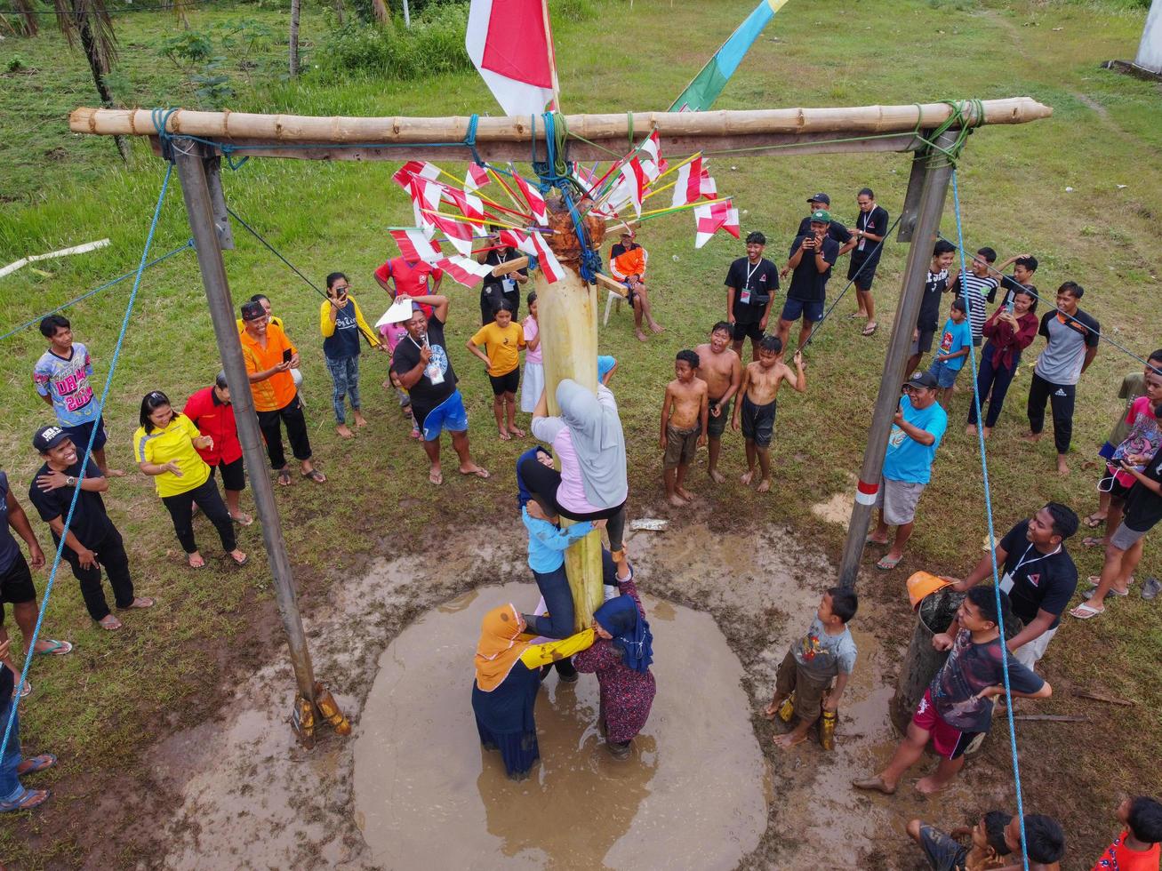 Blitar, Indonesia - September 11th 2022 Aerial view of housewife who is taking part in a banana tree climbing competition to get a prize and is seen by many people photo